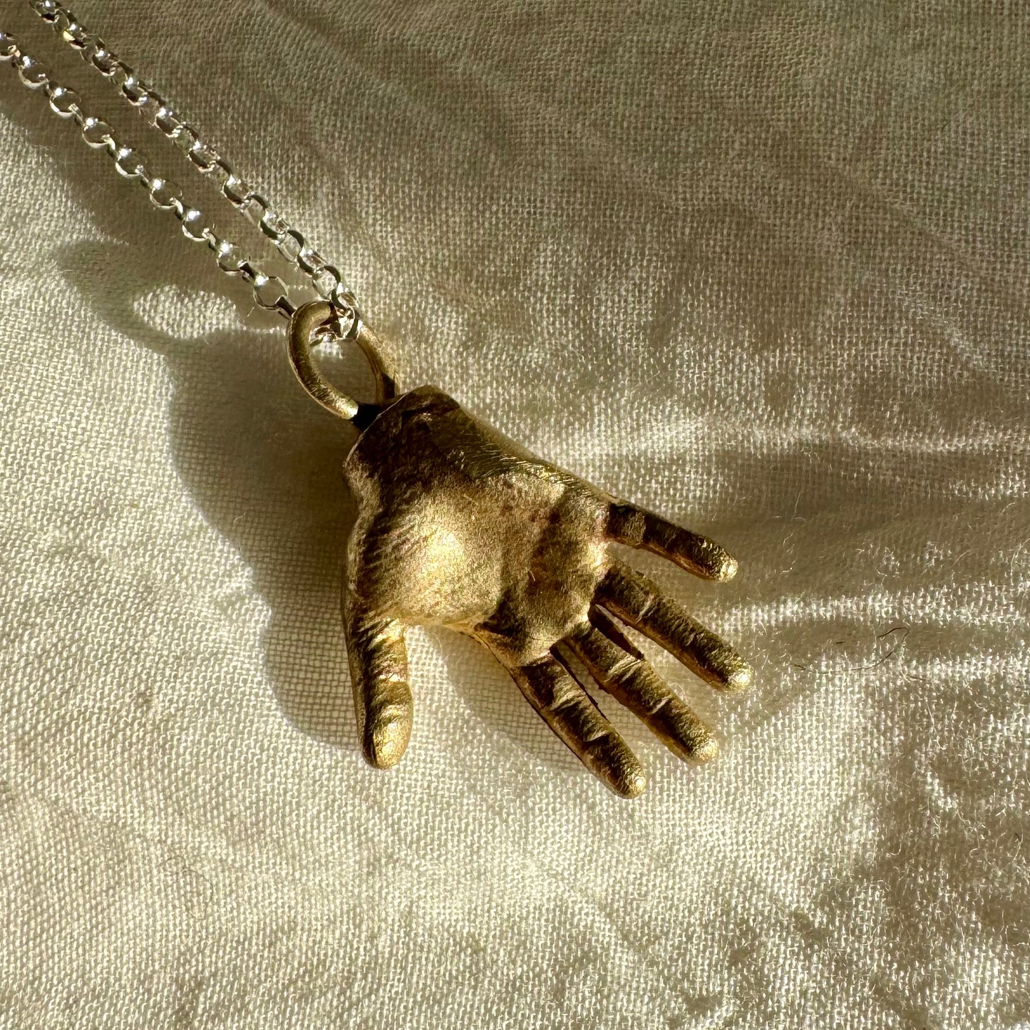 A little Hand charm cast in recycled brass and measuring 2cm by 1.5cm hanging on a 45cm recycled silver chain.