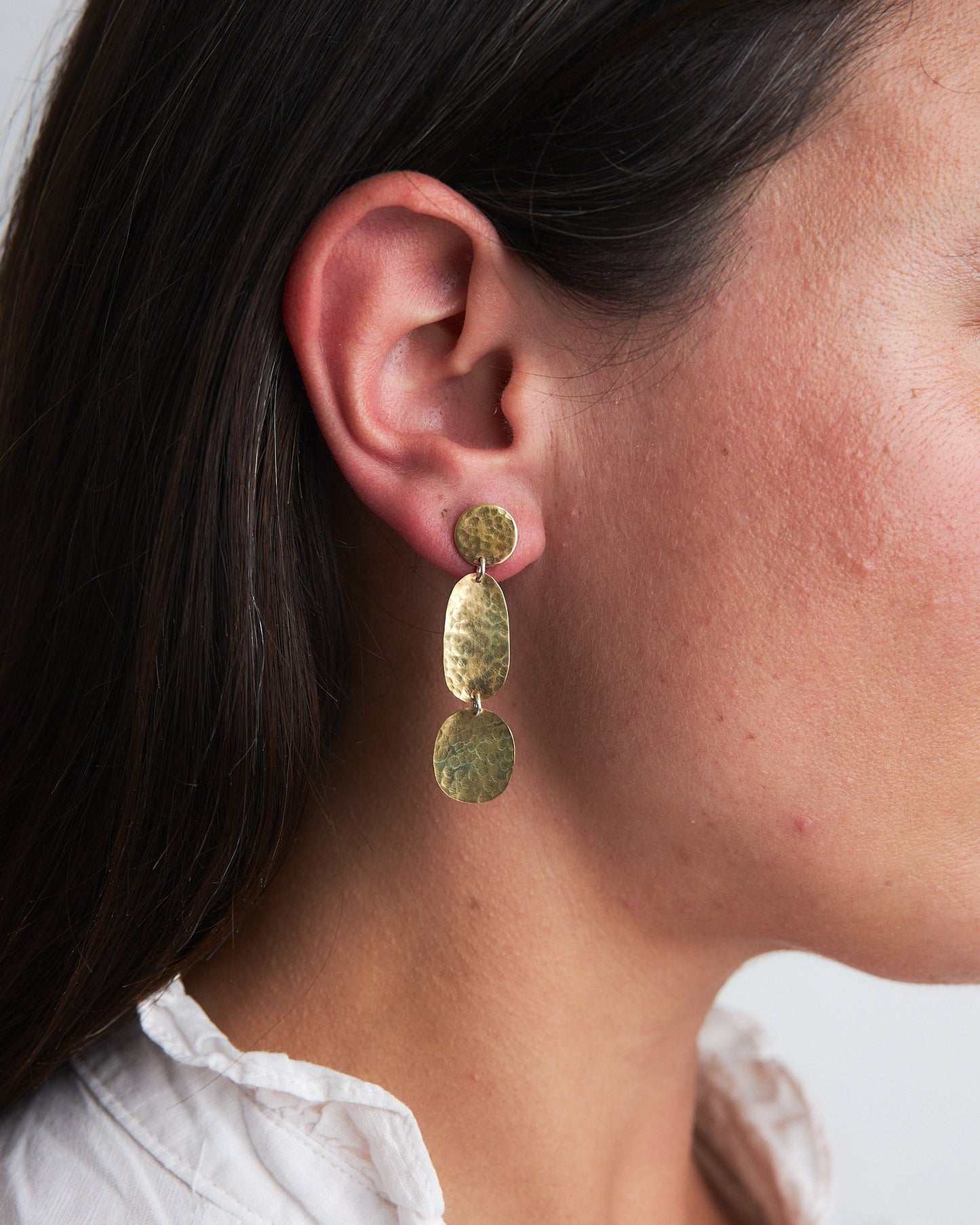 Sea Pebble Earrings: handmade in recycled brass these earrings have three pebble shapes articulated to move as you do. Worn by a model.