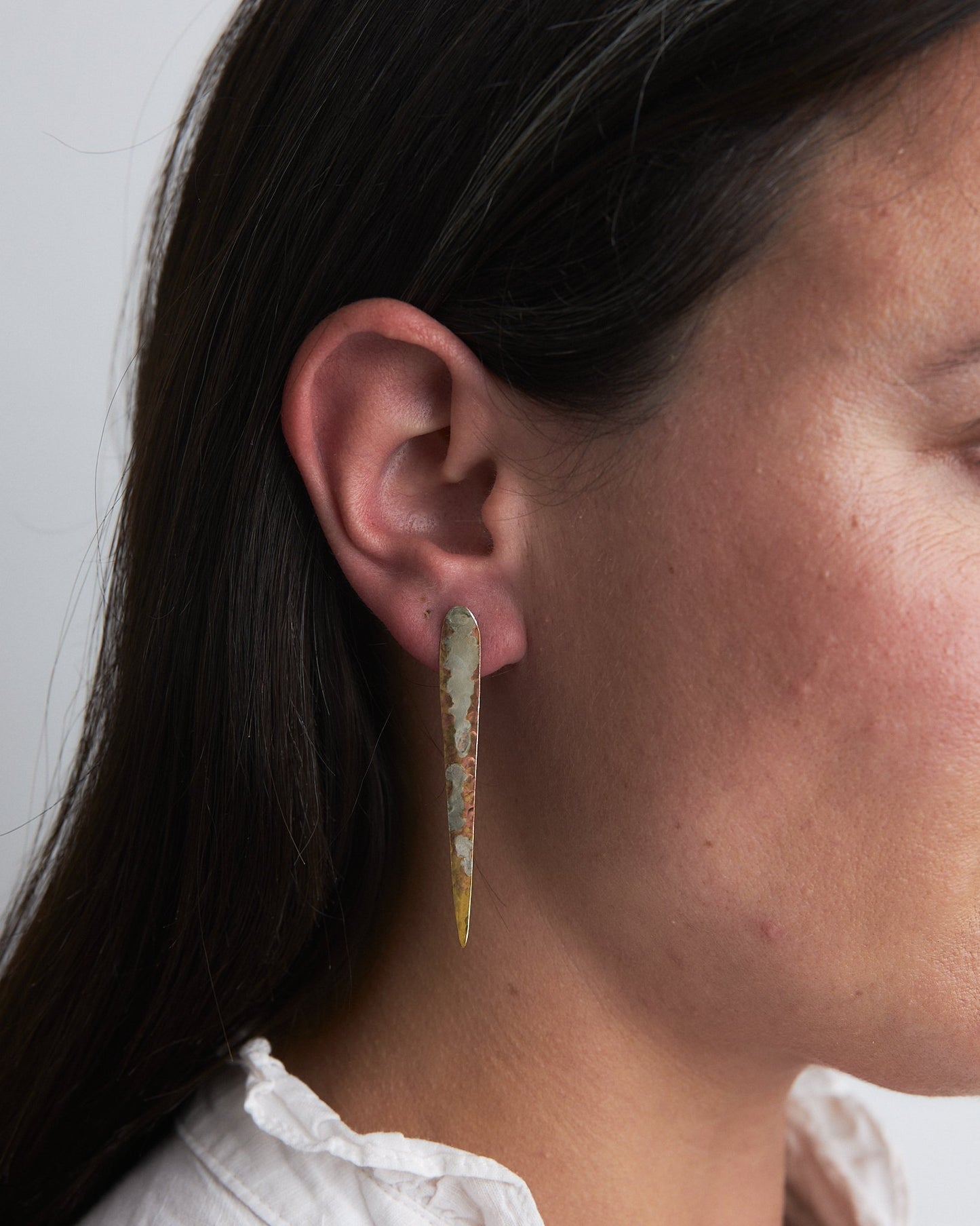 Sea Lichen Shards: handmade earrings in recycled brass with a mother silver patina inspired by lichen on the rocks by the sea. Worn by a model.
