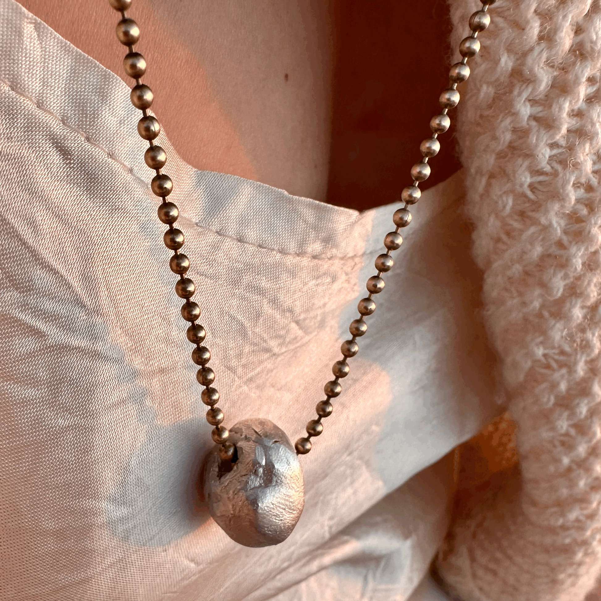 A solid silver hag stone pendant on a brass chain, worn by a model.