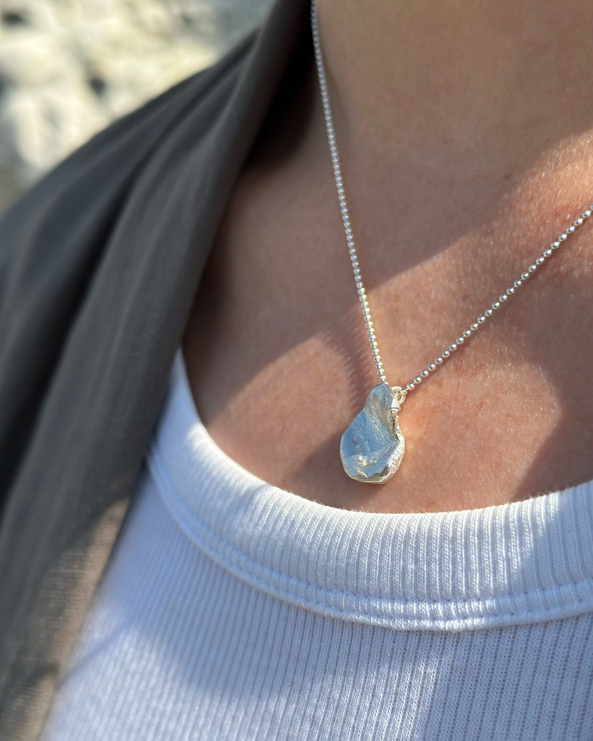 Droplet Necklace: a cast droplet of solid recycled silver on a recycled silver chain. Worn by a model.