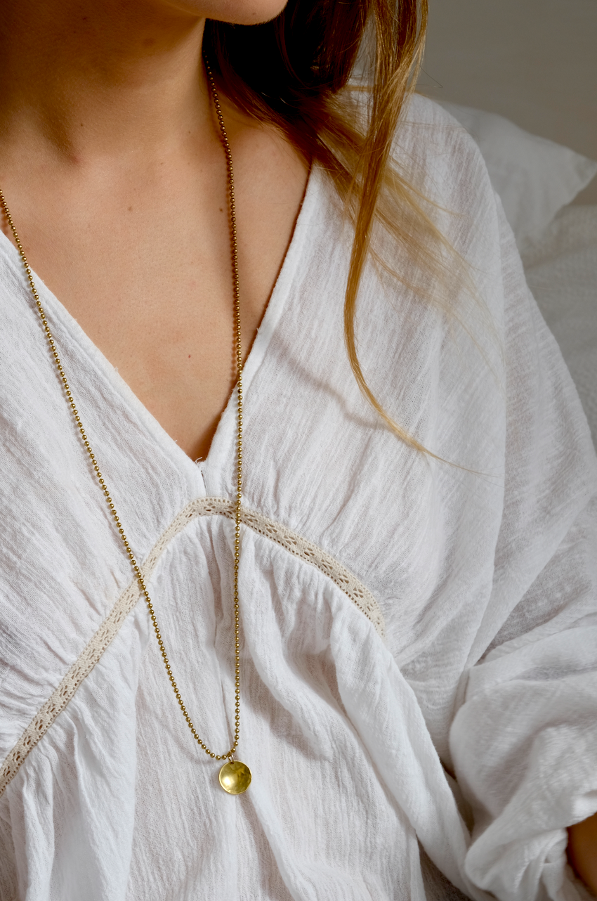 Sunny Pendant: a gorgeous pendant with a tactile hammered and slightly domed brass disc on a vintage brass ball chain - inspired by the sun. Handmade sustainably in Suffolk. Worn by a model.