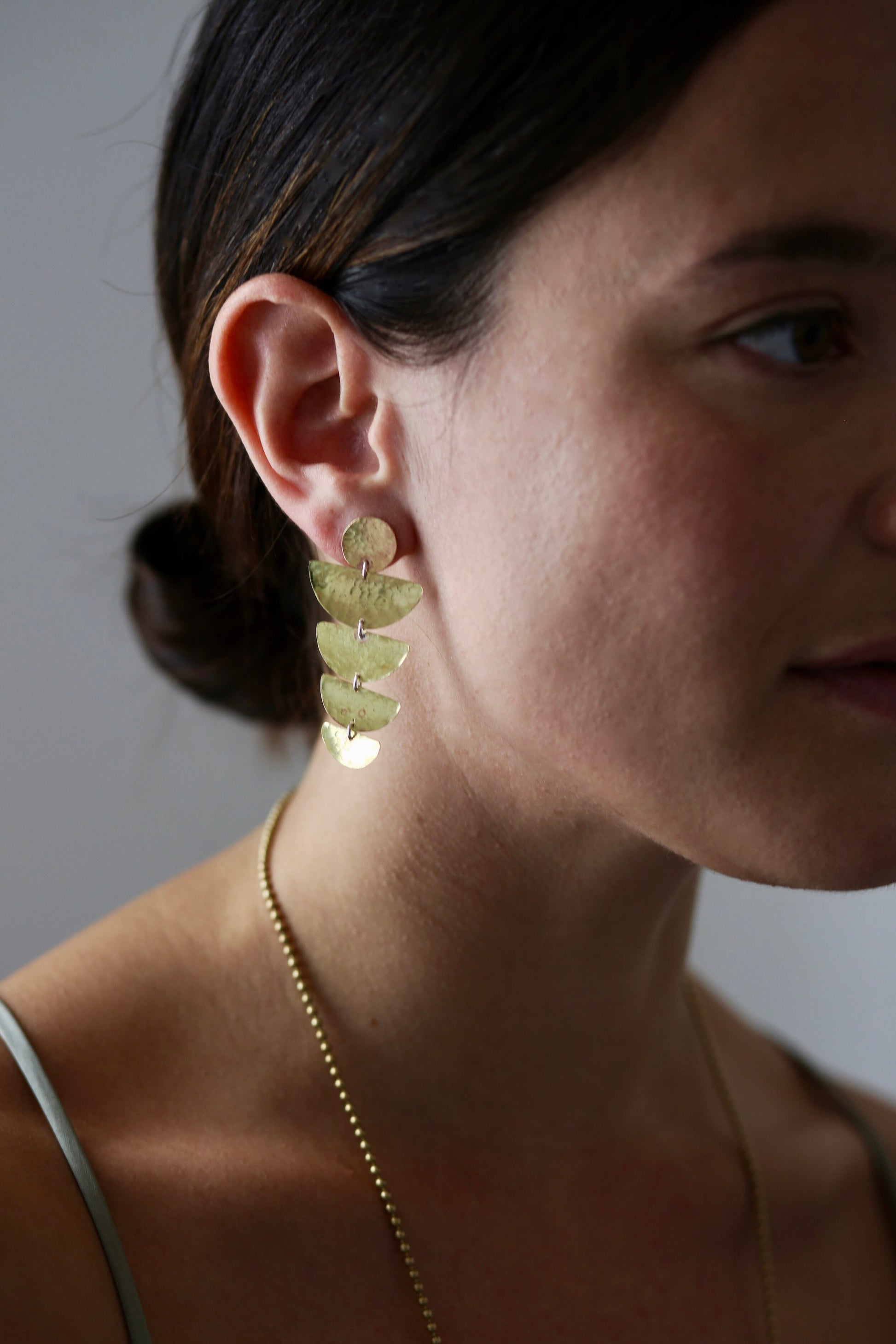 Bella Earrings: handmade with four graduated half moon shapes in recycled brass hanging from a brass disc, worn by a model.