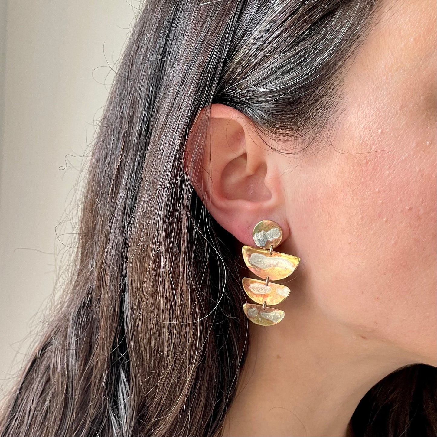 Lyla Earrings: handmade brass earrings with three half moon shapes in brass with molten swirls of recycled silver. Worn by a model.