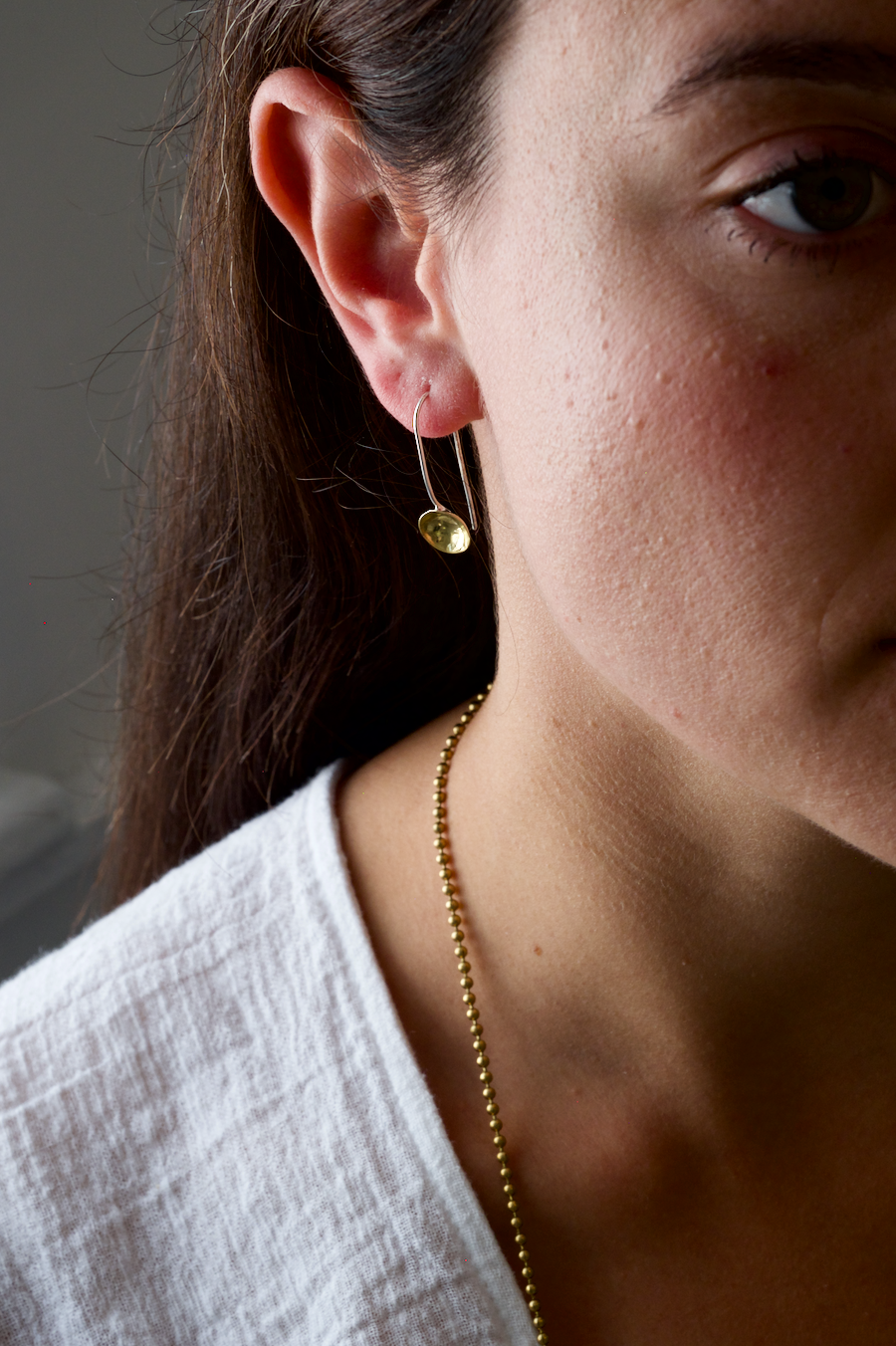 Lara Earrings: Recycled brass earrings consisting of bowl shapes on recycled silver wires. Worn by a model.