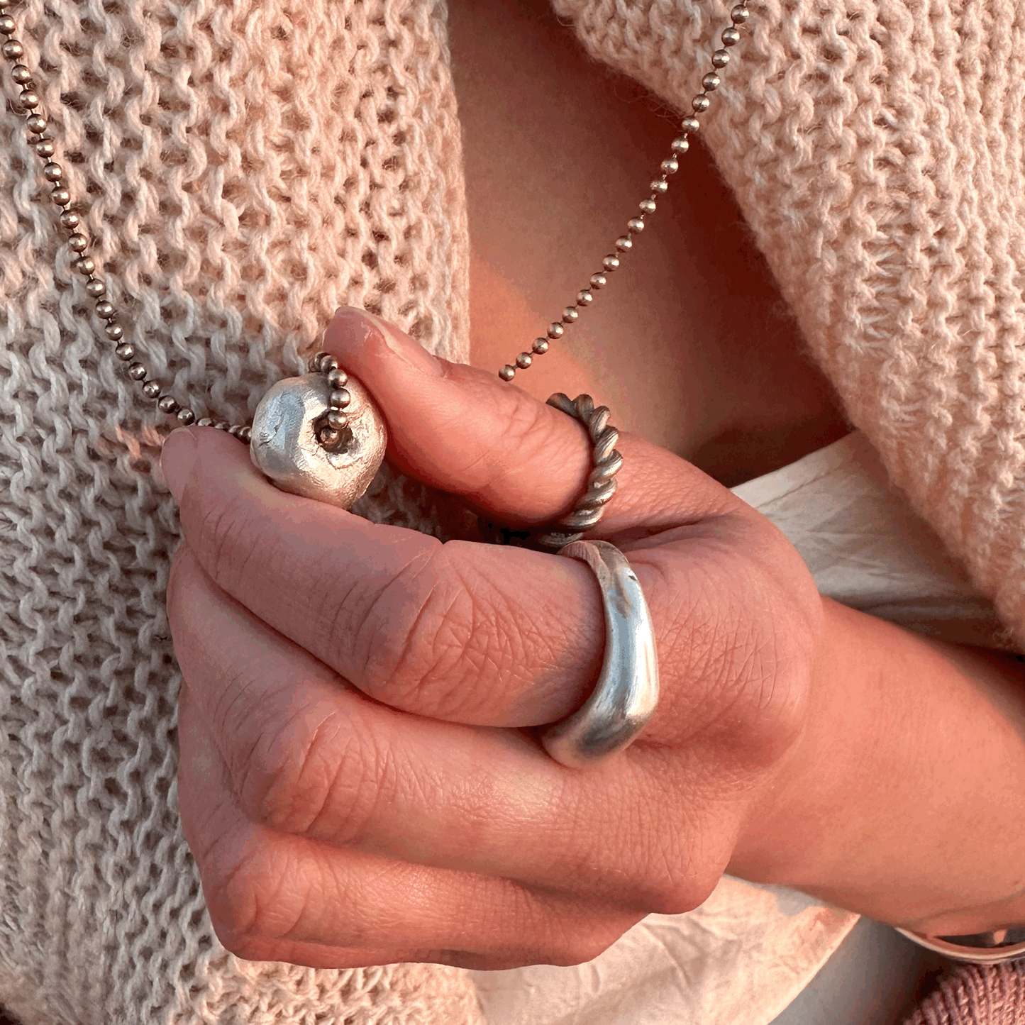 A solid silver hag stone pendant on a brass chain, worn by a model.